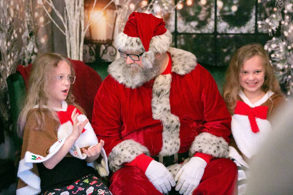 Santa Brett Nichols talks with twins Emily, left, and Alison Johnson, both 8, to see what gifts they want on Dec. 4, in Monroe. Emily and Alison have taken photos with Santa Brett every year since they were three months old. (Ryan Berry / The Herald)