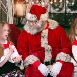 Santa Brett Nichols talks with twins Emily, left, and Alison Johnson, both 8, to see what gifts they want during a photo shoot Sunday, Dec. 4, 2022, in Monroe, Washington. Emily and Alison have taken photos with Santa Brett every year since they were three months old. (Ryan Berry / The Herald)