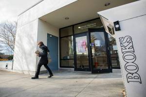 A person walks our of the Edmonds Pop Up Library carrying a book on Thursday, Dec. 15, 2022 in Edmonds, Washington. (Olivia Vanni / The Herald)