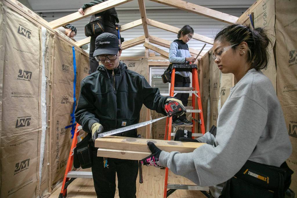 Students Darian Vandee and Angelica Subillaga get their measurements right while working inside a tiny home they and classmates are working on for their pre-apprenticeship program Monday, Dec. 12, 2022, at the Washington Aerospace Training & Research Center in Everett, Washington. (Ryan Berry / The Herald)