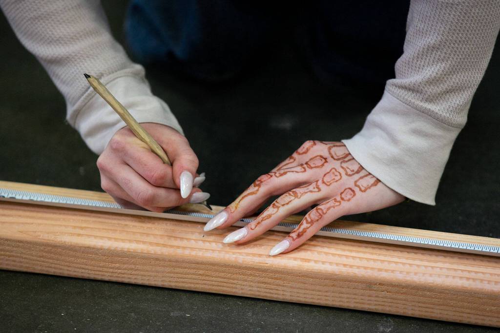 Ellie Fongemie measures cuts on a two-by-four while working on a tiny home for her AMSC pre-apprenticeship program Monday, Dec. 12, 2022, at the Washington Aerospace Training & Research Center in Everett, Washington. (Ryan Berry / The Herald)