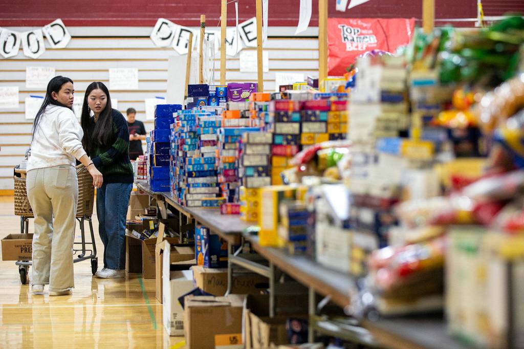 Students make their way through aisles of food and other goods while filling boxes for families during Cascades annual holiday food drive Wednesday, Dec. 14, at Cascade High School in Everett. (Ryan Berry / The Herald)