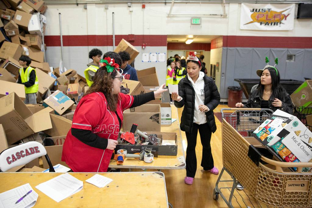 Bethany Rickard, an AP U.S. history and AP human geography teacher at Cascade, helps keep the line moving as volunteers fill boxes with food during Cascades annual holiday food drive Wednesday, Dec. 14, at Cascade High School in Everett. (Ryan Berry / The Herald)