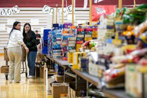 Students make their way through aisles of food and other goods while filling boxes for families during Cascade’s annual holiday food drive Wednesday, Dec. 14, 2022, at Cascade High School in Everett, Washington. (Ryan Berry / The Herald)