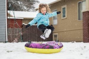 Halle Lucas-Roberts, 6, leaps onto her tube while sledding in front of her home on Tuesday, Dec. 20, 2022 in Everett, Washington. (Olivia Vanni / The Herald)