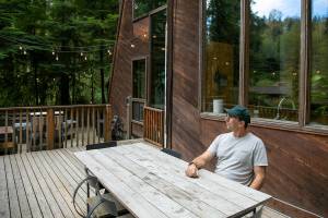 Co-owner Andy Whitcomb sits on the deck behind Cabin 1 at Canyon Creek Cabins on Friday, Sep. 23, 2022, in Granite Falls, Washington. (Ryan Berry / The Herald)