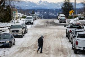 A pedestrian navigates compact snow and ice while crossing the street on Thursday, Dec. 22, 2022 in Everett, Washington. (Olivia Vanni / The Herald)