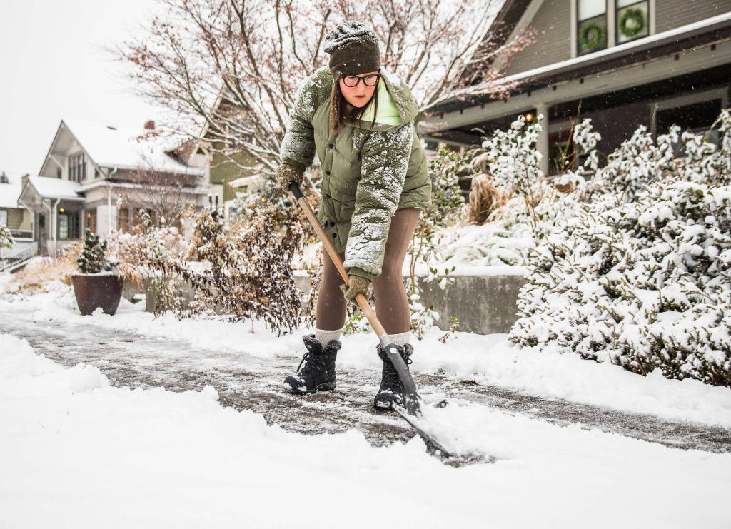 Carly McGinn shovels the sidewalk in front of her home as snow falls on Tuesday, Dec. 20, 2022 in Everett, Washington. (Olivia Vanni / The Herald)