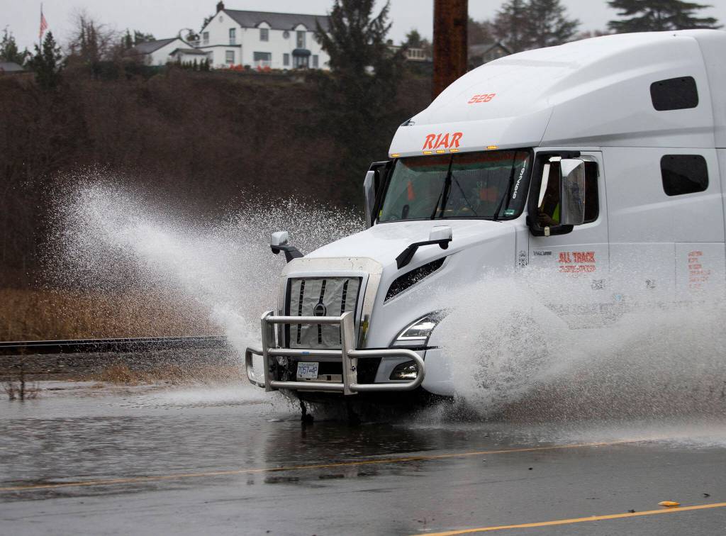 A semi truck sprays water as it drives along a flooded Marine View Drive on Tuesday, Dec. 27, 2022 in Everett, Washington. (Olivia Vanni / The Herald)