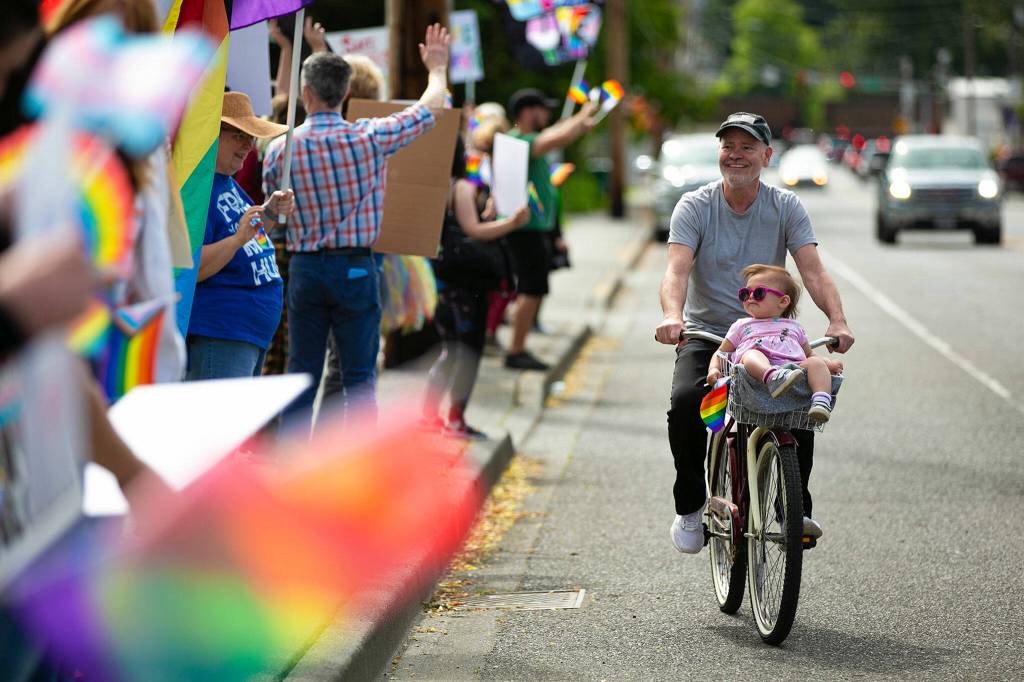 One-year-old Amiyah and her grandfather Bob ride by on a bicycle during a rally in support of LGBTQ+ students on Monday, June 6, 2022, in front of the Marysville School District Service Center in Marysville, Washington. Parents, teachers and students in the district gathered outside the service center to protest a proposal that would have required students to receive parental consent to join extra-curricular clubs, which some felt would pressure LGBTQ+ students into coming out to their parents against their will. (Ryan Berry / The Herald)