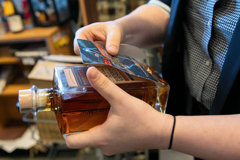 Luin Loeffelbein puts a tater sticker on a bottle of Woodinville Whisky Co.s bourbon on Oct. 13, 2022, in Everett. (Ryan Berry / The Herald)