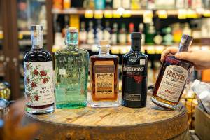 From left, Wild Roots flavored vodka, La Gritona Tequila Reposado, Woodinville Bourbon, Brockmans Gin and Coopers' Craft Bourbon sit on a cask on Thursday, Oct. 13, 2022, at the Evergreen QFC liquor section in Everett, Washington. (Ryan Berry / The Herald)