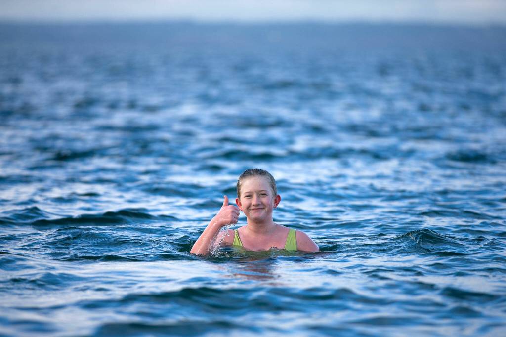 Caroline Bernatek, 12, gives a thumbs-up from the roughly 46-degree Pacific water as she tries to see how long she can last during the 2023 Edmonds Polar Bear Plunge on Sunday, Jan. 1, 2023, at Bracketts Landing in Edmonds, Washington. Bernatek has a running bet with her cousin and receives a dollar for every minute spent in the frigid water. (Ryan Berry / The Herald)