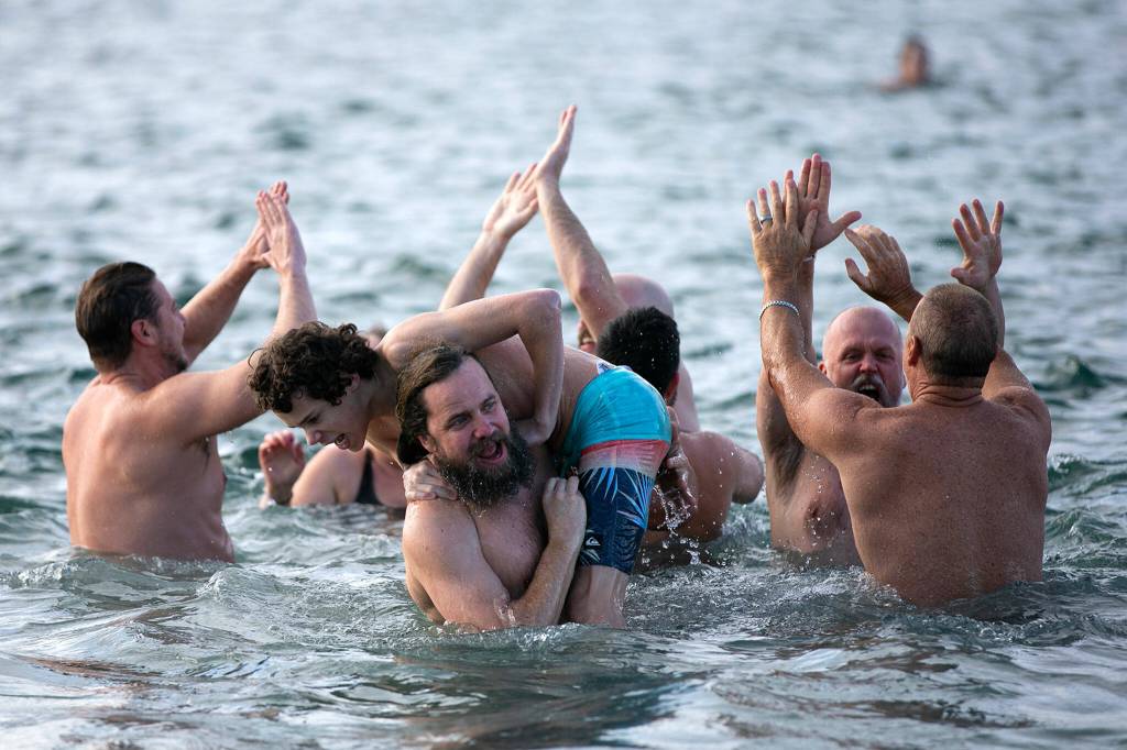 A group of plungers celebrate their bravery during the 2023 Edmonds Polar Bear Plunge on Sunday, Jan. 1, 2023, at Bracketts Landing in Edmonds, Washington. (Ryan Berry / The Herald)