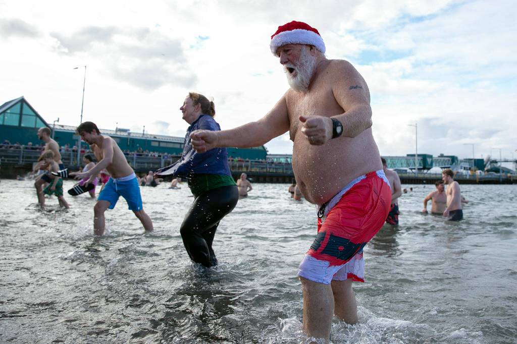 Santa Claus heads for the shore after taking a dip in the Sound during the 2023 Edmonds Polar Bear Plunge on Sunday, Jan. 1, 2023, at Bracketts Landing in Edmonds, Washington. (Ryan Berry / The Herald)