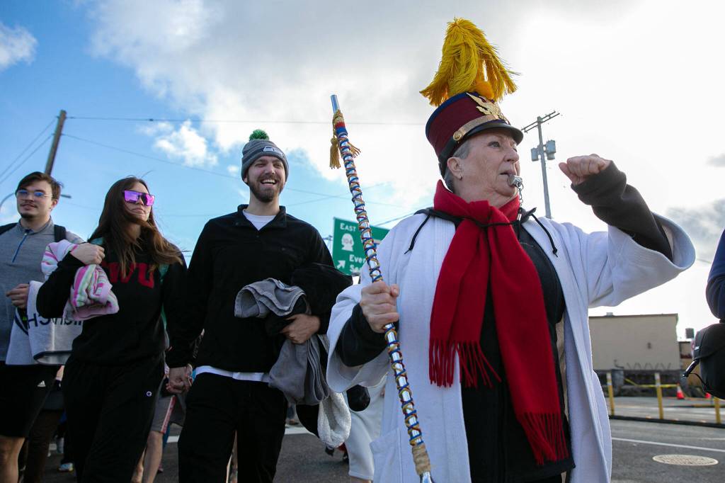 Edith Farrar blows a whistle and leads well over a hundred people to the waterfront during the 2023 Edmonds Polar Bear Plunge on Sunday, Jan. 1, 2023, at Bracketts Landing in Edmonds, Washington. (Ryan Berry / The Herald)