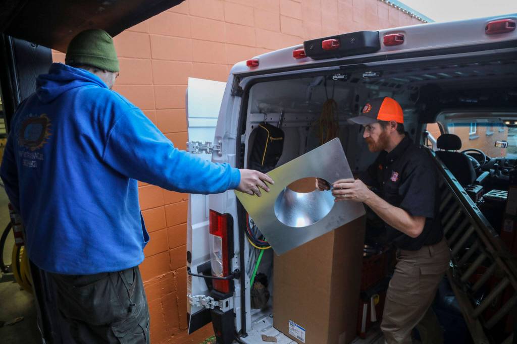 Nick Larsons, 40, left, passes Nick Cairus, 38, items to put in the van at Fast Track Hvac in Stanwood on Monday. Nick Cairus and Patricia Cairus lost their housing in the recession and were homeless for a number of years. They started a successful HVAC company during the pandemic in a former newspaper printing building. (Annie Barker / The Herald)