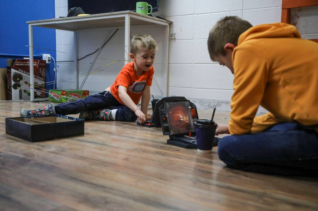 Askel Carius, 6, left, and his brother Jadon Carius, 12, right, play Battleship at Fast Track Hvac in Stanwood on Monday. Nick Cairus and Patricia Cairus lost their housing in the recession and were homeless for a number of years. They started a successful HVAC company during the pandemic in a former newspaper printing building. (Annie Barker / The Herald)