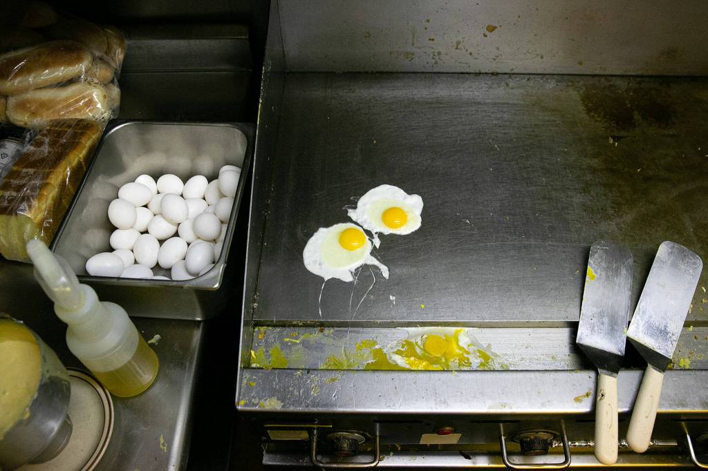 A pair of over easy eggs cook away on the flat top during lunch service at Totem Family Diner on Saturday, in Everett. (Ryan Berry / The Herald)