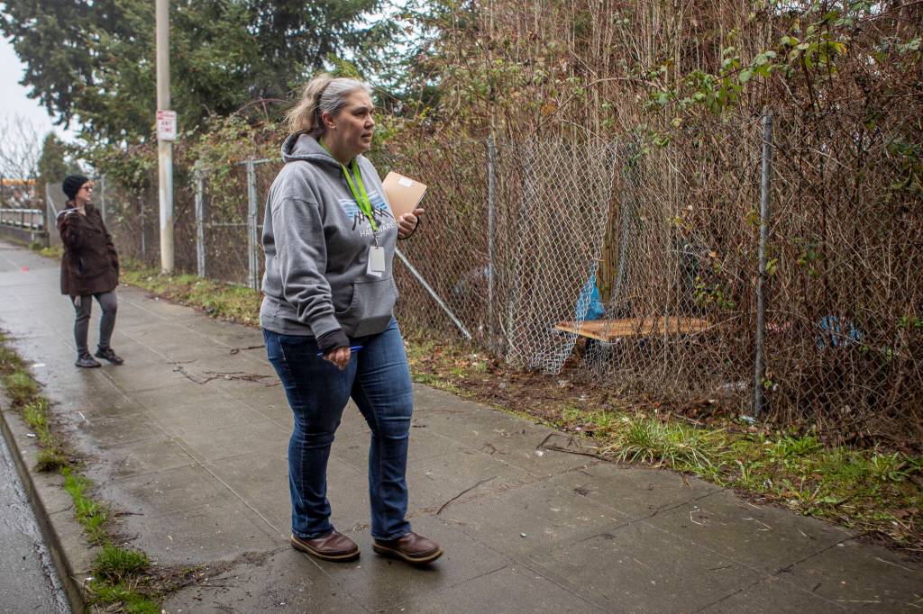 Point-in-time count volunteer Saffron Coelho, left, and Catholic Community Services NW Director of Housing Services and Everett Family Center Director Rita Jo Case, right, cross a street under an overpass during a census of people facing homelessness on Tuesday, in Everett. (Annie Barker / The Herald)