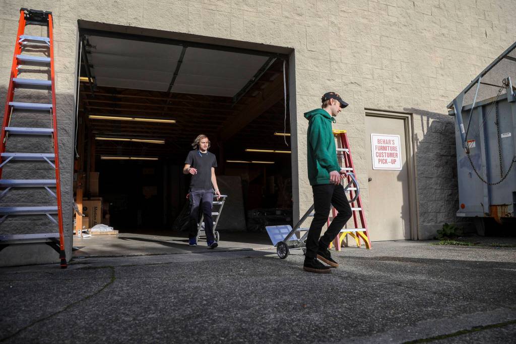 Warehouse associate Brandon Davis, 25, right, wheels a dolly while unloading a truck of recliners at Behars Furniture on Monday. Behars Furniture on Broadway in Everett is closing up shop after 60 years in business. The family-owned furniture store opened in 1963, when mid-century model styles were all the rage. Second-generation owner, Jay Behar says its time to move on. (Annie Barker / The Herald)