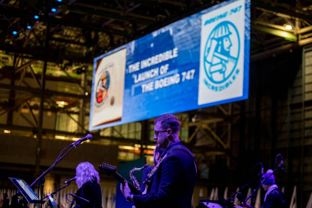 A band performs while videos play detailing the Boeings history on Tuesday during a celebration of the final 747 in Everett. (Annie Barker / The Herald)