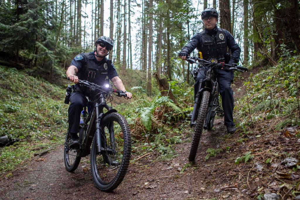 Police officers JJ Voeller, left, and Kyle OHagan, right, pose for a photo on new electric-assisted mountain bikes Sunday near the Mountlake Terrace Police Department. (Annie Barker / The Herald)