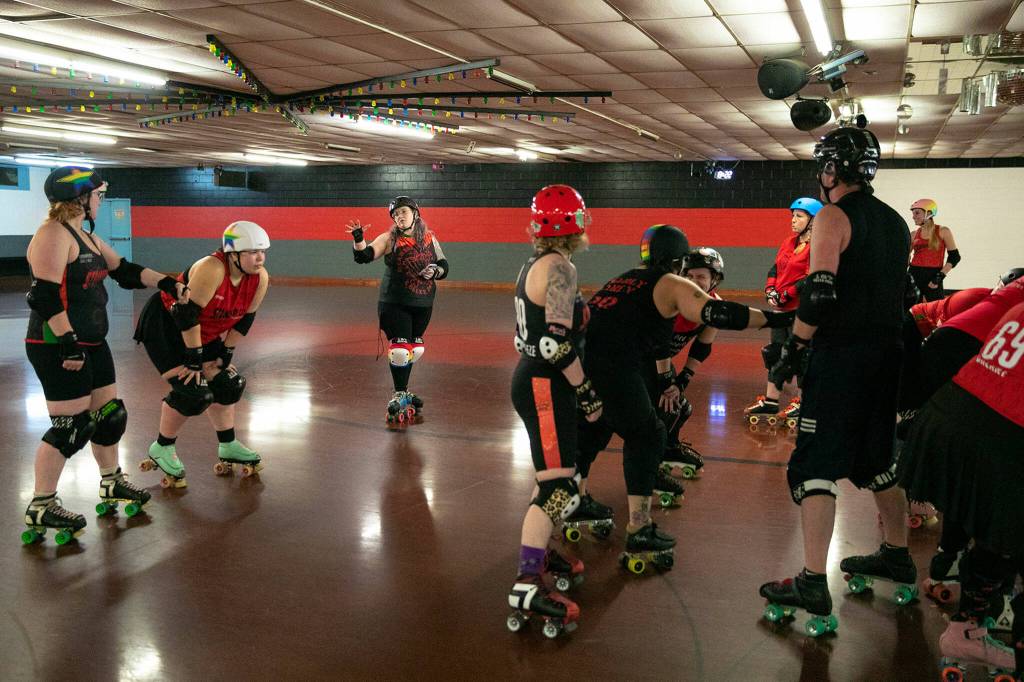 Members of Strawberry City Roller Derby listen to coach Melvin Dictive Mel Viehouser-McGuire, third from left, while going through some practice jams at Marysville Skate Center on Monday, Feb. 6, in Marysville. (Ryan Berry / The Herald)