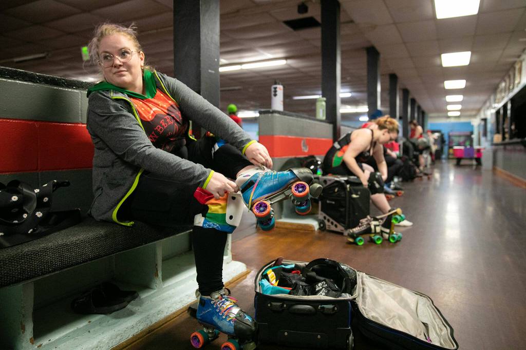 Head coach Melvin Dictive Mel Viehouser-McGuire, who has been participating in roller derby for nine years, puts on skates before leading Strawberry City Roller Derby in practice at Marysville Skate Center on Monday, Feb. 6, in Marysville. (Ryan Berry / The Herald)