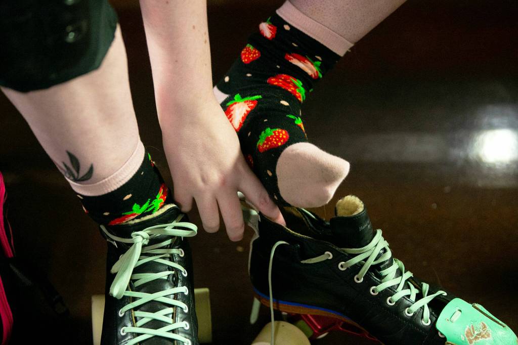 Rina Rock You Marina Kolbeck dons strawberry socks while putting on gear during a Strawberry City Roller Derby practice at Marysville Skate Center on Monday, Feb. 6, in Marysville. (Ryan Berry / The Herald)