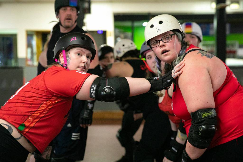 Rose Misconduct Ciara Jay, left, and Jess-Trippin Jessica Rigel look over to their coach before the start of a jam during a Strawberry City Roller Derby practice at Marysville Skate Center on Monday, Feb. 6, in Marysville. (Ryan Berry / The Herald)