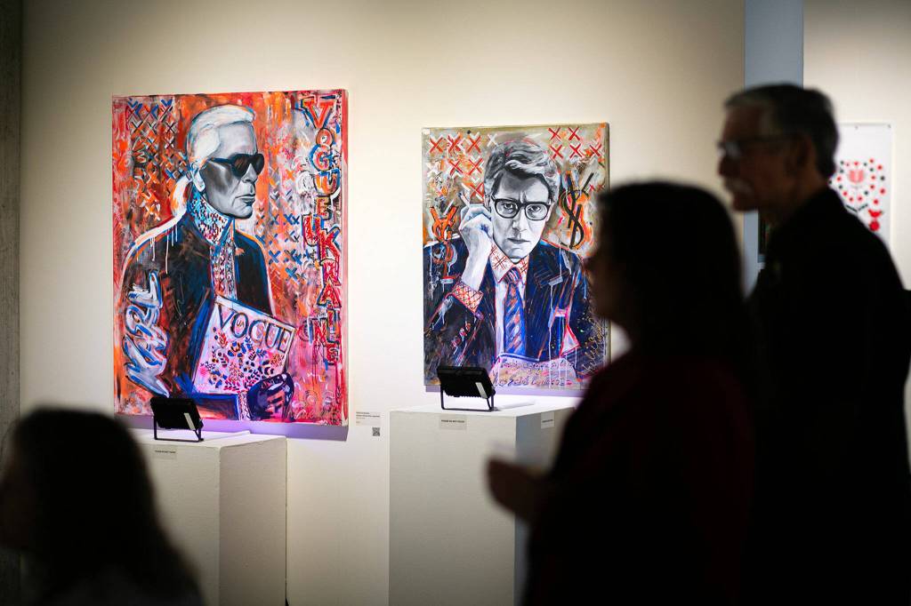 People watch a video installation while standing near a pair of paintings by Yuliia Kravchenko during a public event highlighting the For Ukraine: Art of Freedom exhibit at the Schack Art Center on Saturday, in downtown Everett. (Ryan Berry / The Herald)