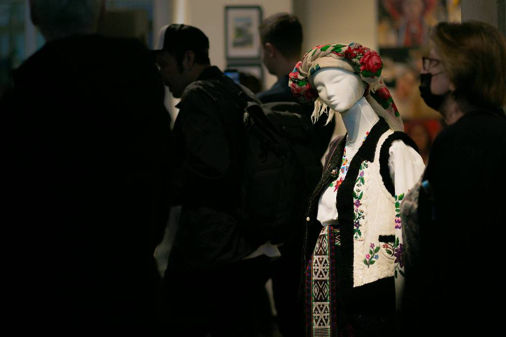 A mannequin donning traditional Ukrainian bridal attire is illuminated as a crowd gathers to listen to a live music performance during a public event highlighting the For Ukraine: Art of Freedom exhibit at the Schack Art Center on Saturday, in downtown Everett. (Ryan Berry / The Herald)