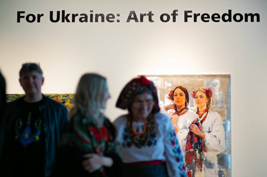 Guests filter through the gallery past a wall of paintings during a public event highlighting the For Ukraine: Art of Freedom exhibit at the Schack Art Center on Saturday, in downtown Everett. (Ryan Berry / The Herald)