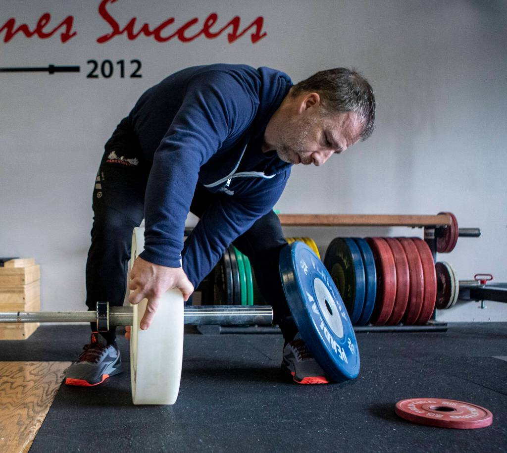 Paramount Strength and Conditioning owner and head weightlifting coach Chris Douglas, 41, adjusts weights with Phil Arnold, 74, at Paramount Strength and Conditioning in Mountlake Terrace, Washington on Thursday, Feb. 2, 2023. Arnold is 74 and recently retired as an attorney. He took up weightlifting after retirement and recently won a national championship. (Annie Barker / The Herald)