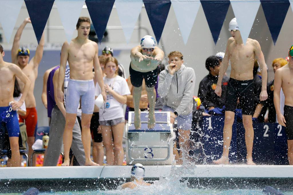Woodinville junior Carter Johnson dives in as teammate Alex Popov finishes his leg during the 200 yard freestyle relay consolation race at the 4A WIAA Boys High School Swim and Dive Championships on Friday, Feb. 18, 2023, at the Weyerhaeuser King County Aquatic Center in Federal Way, Washington. (Ryan Berry / The Herald)