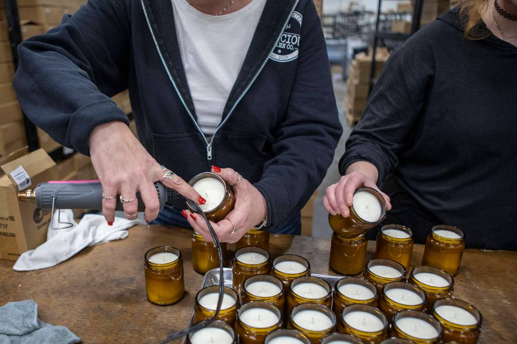 Owner and CEO Lacie Carroll, left, and creative director Kacie Kicinski, right, check candles and smooth out the tops at the Malicious Women Candle Co workspace on Feb. 15 in Snohomish. The business is women run and owned. (Annie Barker / The Herald)