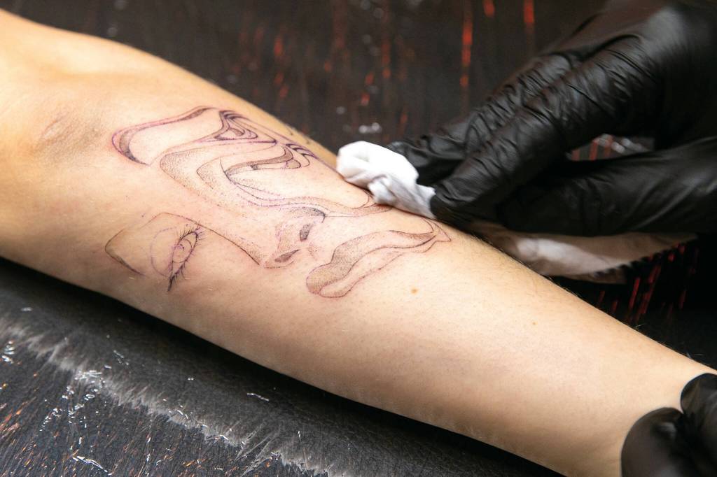 Hurtado wipes down Cheyenne Stultzs arm. Fine line artists such as Hurtado use single needles to create softer, more intricate-looking portraits. (Ryan Berry / The Herald)