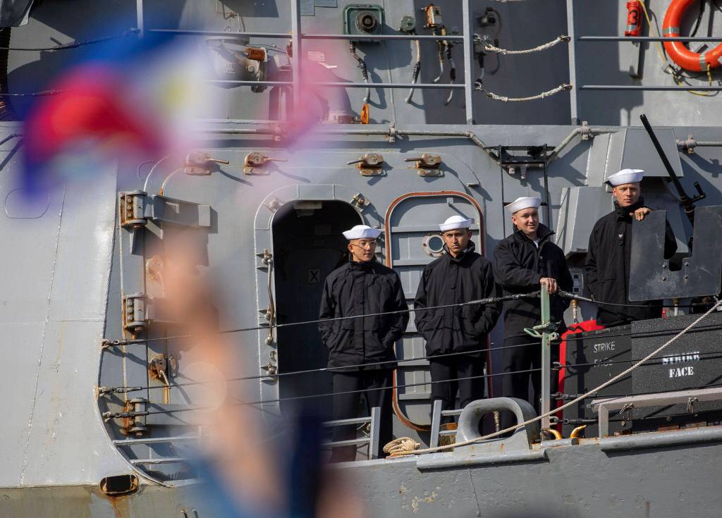 Families wave flags to people onboard the USS Barry in Everett, Washington on Friday, March 17, 2023. The USS Barry arrived to its new homeport at Everett Naval Station, previously from Yokosuka, Japan. The crew is led by Commanding Officer, Cmdr. Grant Bryan. (Annie Barker / The Herald)