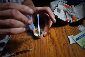 An addict prepares heroin, placing a fentanyl test strip into the mixing container to check for contamination, Wednesday Aug. 22, 2018, in New York. If the strip registers a "pinkish" to red marker then the heroin is positive for contaminants. (AP Photo/Bebeto Matthews)