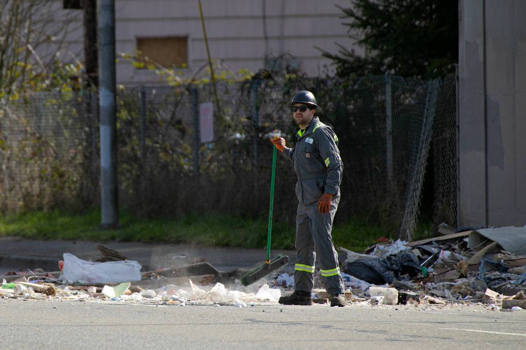 A heavy tow operator begins to sweep debris from Everett Avenue after a semi carrying trash crashed and spilled its contents from I-5 on Thursday, March 16, 2023, in Everett, Washington. (Ryan Berry / The Herald)