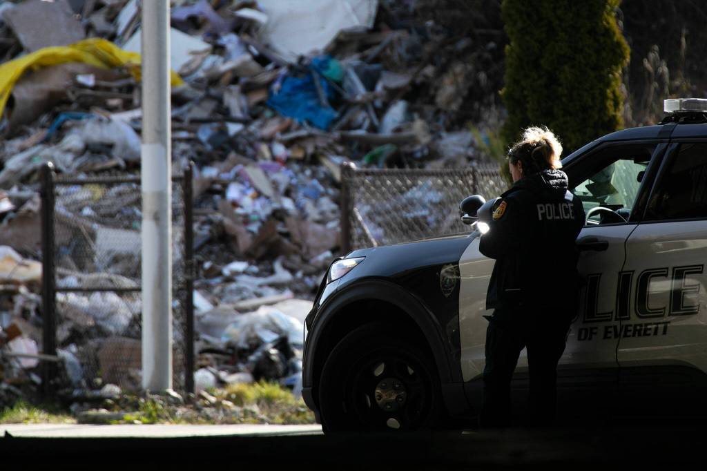 An Everett Police officer checkers her phone while tending to the scene of a late morning crash on I-5 that left a semi filled with trash hanging above Everett Avenue on Thursday, March 16, 2023, in Everett, Washington. (Ryan Berry / The Herald)