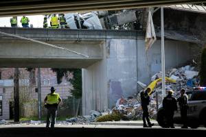 Emergency crews get to work as a semi carrying trash leans over the edge of I-5 northbound after a late morning crash above Everett Avenue on Thursday, March 16, 2023, in Everett, Washington. (Ryan Berry / The Herald)