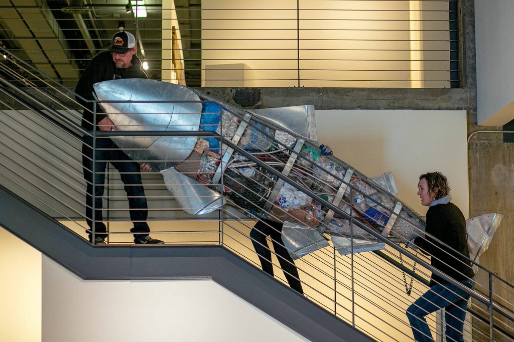 Artists Pieter and Lucy VanZanden haul a giant metal fish upstairs during the installation of Exploring The Edge at Schack Art Center on Sunday, March 19, 2023, in Everett, Washington. The fish, part of their three-piece ҃onsumption,Ӡis made from salvaged material and filled with single-use plastics that the couple have accumulated at home over the past five years. (Ryan Berry / The Herald)