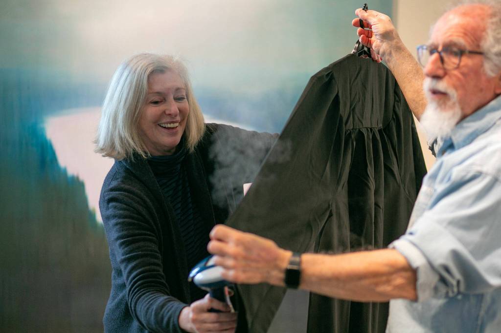 Meg Holgate, with the helping hand of fellow guest curator Steve Klein, steams a set of judicial robes while working on some of the more detailed work of installing A Precarious Edge at Schack Art Center on Sunday, March 19, 2023, in Everett, Washington. (Ryan Berry / The Herald)