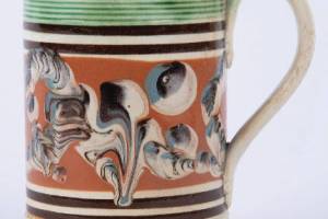 Antique mocha ware, made in England to export to the United States and Canada in the 18th and 19th centuries, caught collectors attention in the mid-20th century. Like many mocha pieces, this colorful mug is decorated with several patterns.
