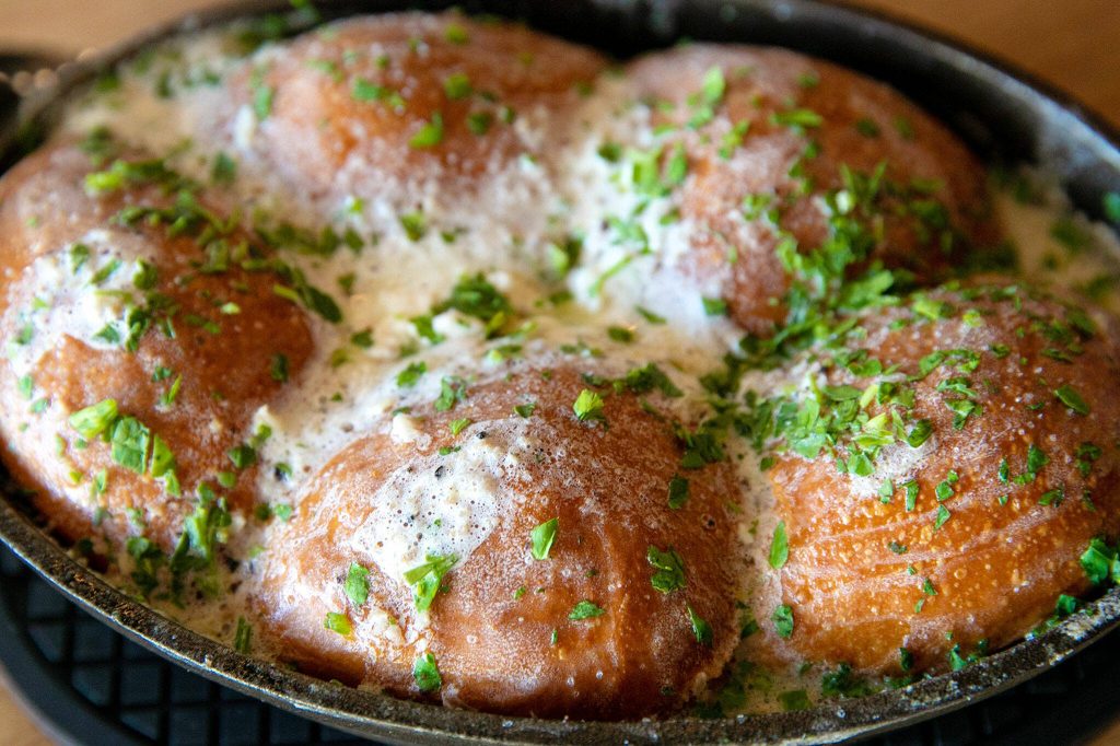 Parker House Rolls are served in a small cast iron dish and doused in truffle butter at Rare Society on Tuesday, April 25, 2023, in Mill Creek, Washington. (Ryan Berry / The Herald)