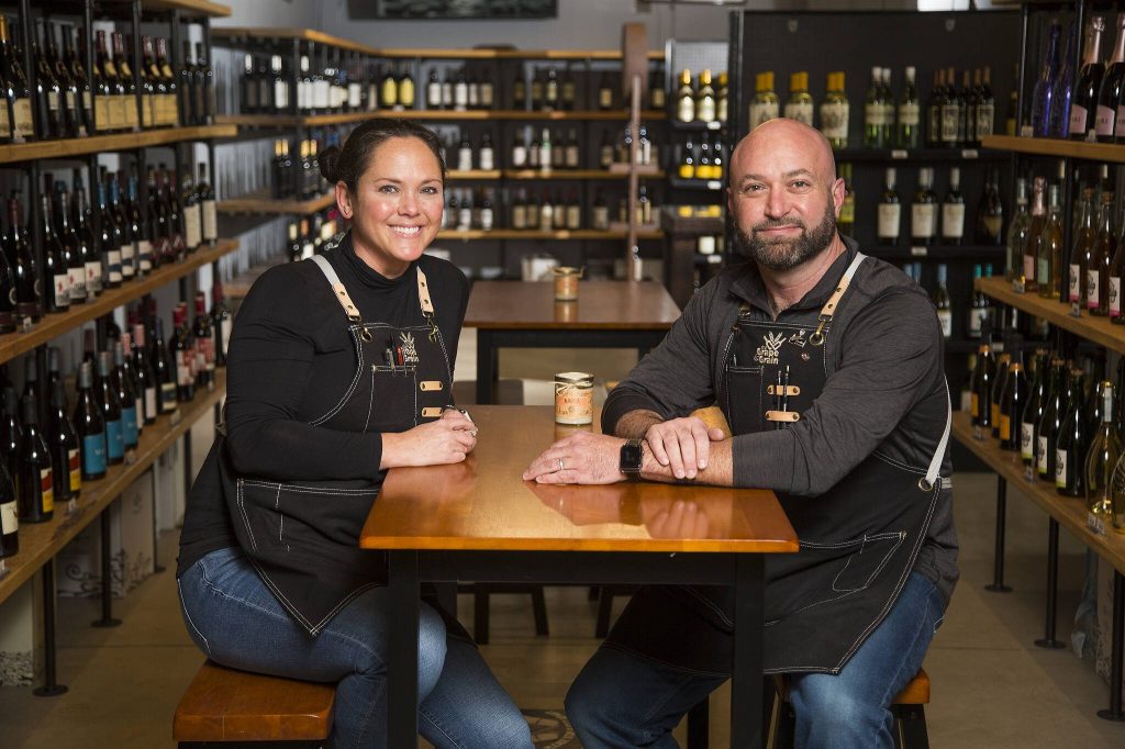 Owners Krista and Eric Brown sit among rows of wines at The Grape & Grain, a new independent beer and wine store on Evergreen Way, on Wednesday, April 28, 2021 in Everett, Washington. (Andy Bronson / The Herald)