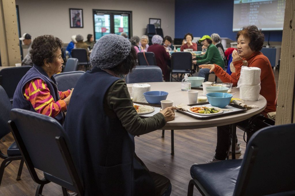 Seung Lee, right, talks to tablemates during a senior community meals program focused on the Korean community at Homage in Lynnwood, Washington on Thursday, May 4, 2023. (Annie Barker / The Herald)