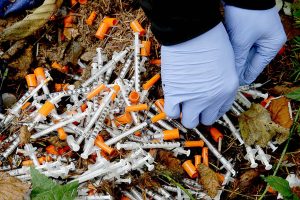 In this Nov. 8, 2017 photo, Steph Gaspar, a volunteer outreach worker with The Hand Up Project, an addiction and homeless advocacy group, cleans up needles used for drug injection that were found at a homeless encampment in Everett, Wash. The number of unsheltered chronically homeless - those who have been homeless for longer than a year while struggling with a serious mental illness, substance use disorder or physical disability - more than doubled in the Everett region since 2015. (AP Photo/Ted S. Warren)